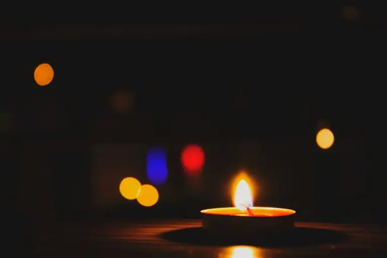 A candle glows warmly in the foreground against a bokeh-filled dark background.